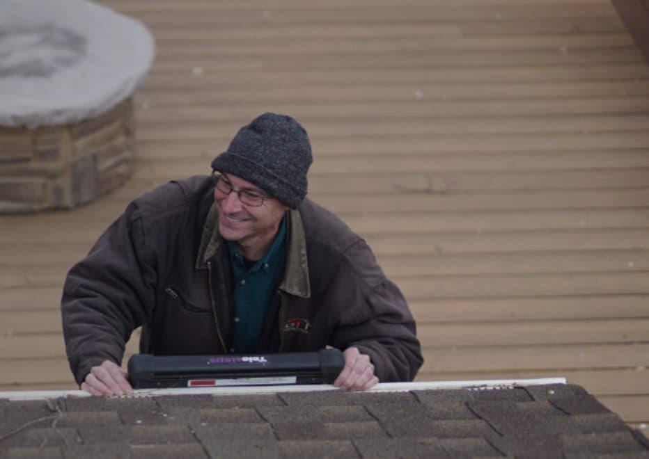 A Scott Home Services inspector coming up a ladder over the edge of a shingled roof